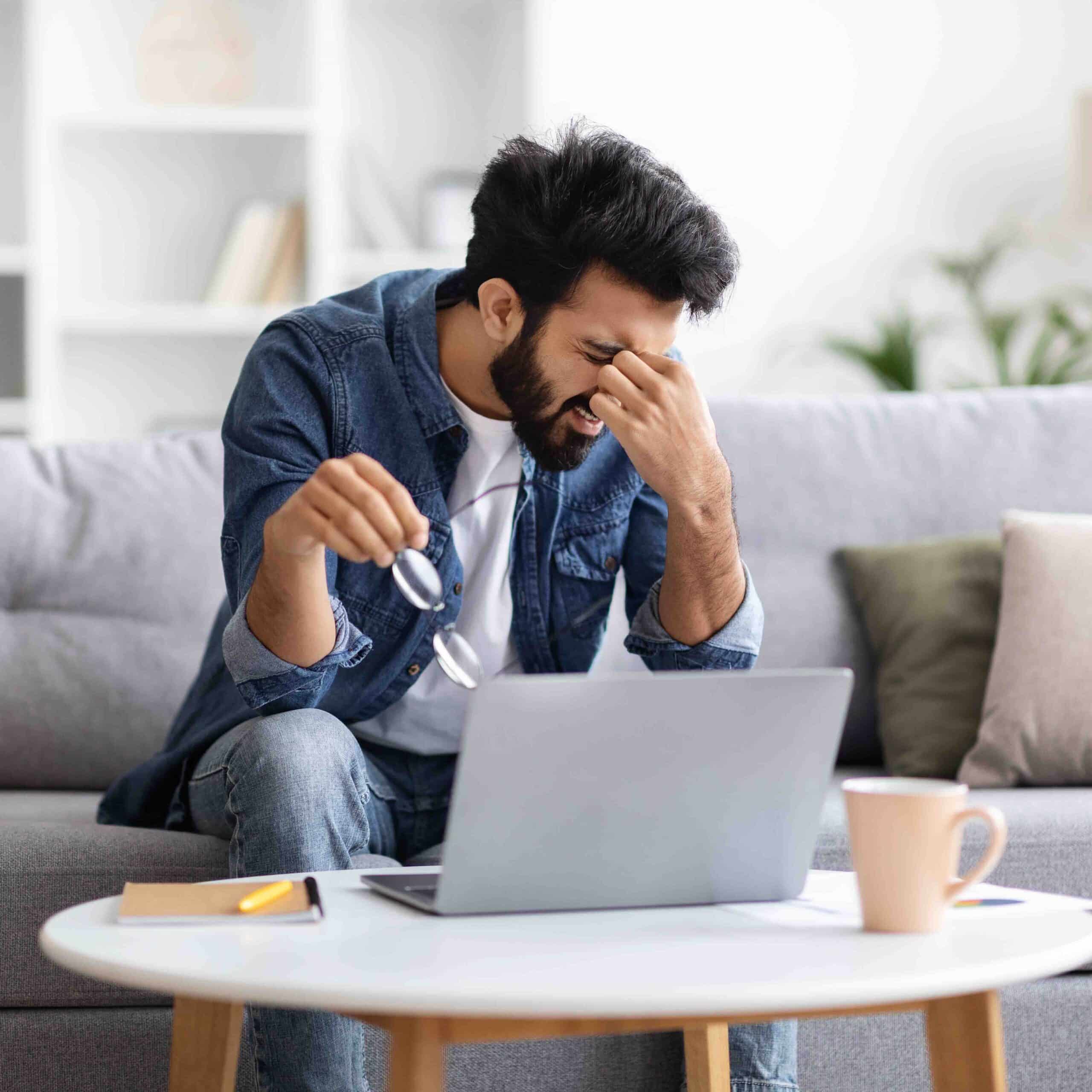 Gestresster Freelancer mit Augenmüdigkeit und störender Brille nach langer Laptop-Arbeit