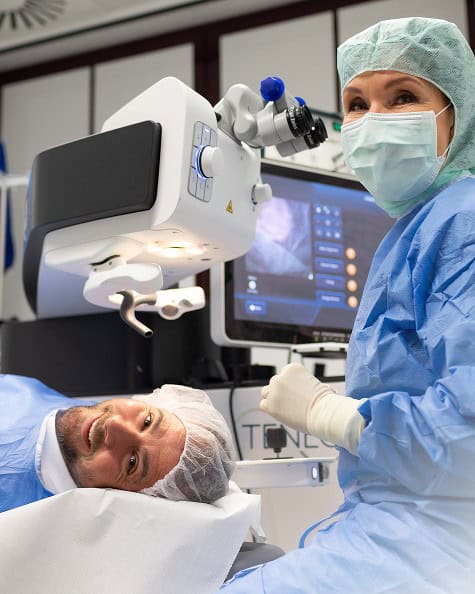 Ärztin bereitet Laserbehandlung vor, Patient liegt auf Behandlungstisch, medizinische Geräte im Hint.